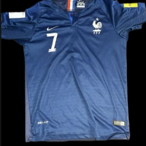 Frankrike Griezmann VM 2018 tröja - Säljer en officiell blå fransk landslagströja från VM 2018 med Griezmann och nummer 7 på ryggen. Tröjan har korta ärmar, FFF-logga, Nike-märke och FIFA Fair Play-patch. Tillverkad i lätt Dri-FIT-material som andas. Storleken är 176, den passar XS och S! Hör av dig vid frågor och funderingar 