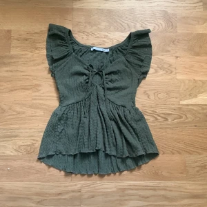 Grön blus med snörning från lager 157 - Supersöt grön blus från lager 157 i storlek XS. Den har volangärmar, snygg snörning och cut-out framtill, samt en ribbad struktur i tyget. Blusen är loose fit och har en peplumliknande form som ger en chill och trendig vibe.