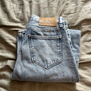 Calvin Klein ljusblå raka jeans - Säljer ett par ljusblå jeans från Calvin Klein med klassisk femficksdesign och tydlig logga på bakfickan. Jeansen har rak passform och hög midja, tillverkade i slitstarkt bomullsjeansmaterial. Perfekta för dig som gillar en clean och tidlös look. W27, L32