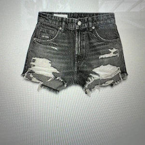 Grå jeansshorts från Zara, strl 36 - Snygga grå jeansshorts från Zara med hög midja och råa, fransiga kanter. Shortsen har slitna detaljer och klassiska fem fickor. Perfekt för dig som gillar en edgy och avslappnad stil. Materialet är robust denim och passformen är loose.