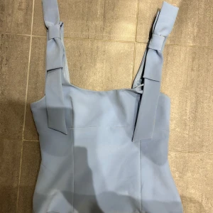 Ljusblå linnetopp med knytband - Supersöt ljusblå linnetopp med breda axelband som knyts i stora rosetter på axlarna. Toppen är croppad och har en stilren, rak passform. Perfekt att matcha med jeans eller kjol.