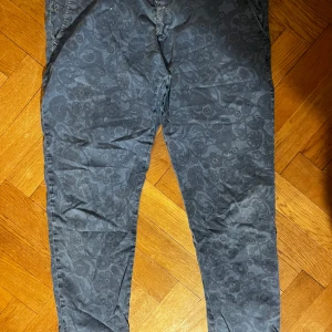 Mörkblå blommiga chinos - Snygga mörkgrå chinos med diskret blommigt mönster. Byxorna har en smal passform.