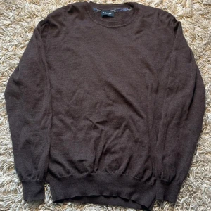 Brun stickad tröja från Sand Copenhagen - Mörkbrun stickad tröja från Sand Copenhagen med rund halsringning och ribbade muddar. Enkel och stilren design som passar perfekt till jeans eller chinos. Skön och mjuk känsla, perfekt för kyligare dagar.