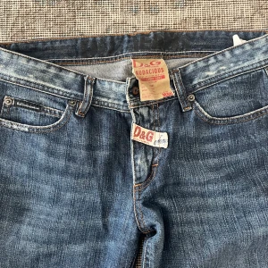 Blå D&G Audacious jeans bootcut - Snygga blå jeans från D&G Audacious med klassisk femficksdesign och coola detaljer som D&G-logga vid fickan och gylfen. Jeansen har bootcut-ben och är gjorda i slitstarkt denim med lätt tvättad look. Perfekt för dig som gillar stilrena och trendiga jeans.