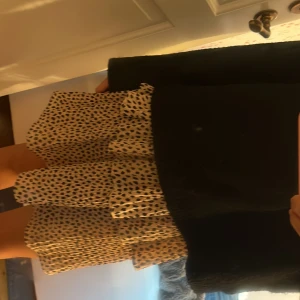 Leopardmönstrad volangkjol Chiara Forthi - Supersöt kort kjol från Chiara Forthi i beige med svart leopardmönster. Kjolen har volanger och ett plisserat tyg som ger en flowy känsla. Elastisk hög midja med guldfärgad logodetalj. Perfekt för dig som gillar trendiga och lekfulla plagg. Dessvärre har logodetaljen lossnat på ena sidan men går enkelt att fixa! 