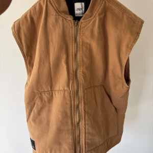 Brun väst från Zara med dragkedja - Säljer en brun väst från Zara i kraftig bomull med rak passform. Västen har två stora fickor framtill och stängs med dragkedja. Perfekt för lager-på-lager och enkel att styla till olika outfits. Är storlek 158 den är väldigt stor i storlek. Jag som är 160 kan få på mig den. Ny pris var 400kr