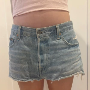 Levis jeanskjol - Midjemått: 40,5 längd: 28,5 Ljusblå jeanskjol från Levi's med klassisk femficksdesign, rå och fransig kant nertill samt knapp- och dragkedjestängning. Ikonisk Levi's-lapp bak i midjan och röd etikett på bakfickan.