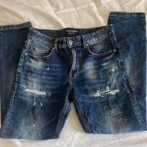 Blå distressed jeans Supply & Demand XS - Snygga blå jeans från Supply & Demand i storlek XS med slitna detaljer, hål och färgstänk för en riktigt edgy look. Klassisk femficksmodell med raka ben, modellen är Slim fit, och de är helt nya🔆