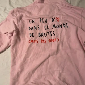 Rosa hoodie från Mira Paris - en superfin rosa hoodie med fransk text på ryggen. Den har en mysig luva och är perfekt för chilliga dagar. Texten är i svart och rött, vilket ger en cool kontrast. Perfekt för dig som vill ha något unikt i garderoben! Använd ca 4 gånger. Nypris 1200. Kom med bud!💘💖