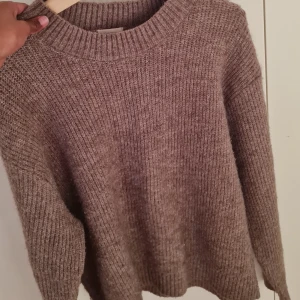 Beige stickad tröja med rund hals - Mysig beige stickad tröja med grov ribbstickning och rund halsringning. Tröjan har långärmade ärmar och en relaxed passform som är perfekt för kyliga dagar. Passar dig som gillar en enkel och stilren look.