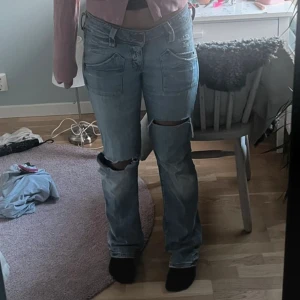 Ljusblå slitna jeans med raka ben - Säljer ett par ljusblå jeans med raka ben och stora slitningar vid knäna. Jeansen har stora framfickor och klassisk knappgylf. De är tillverkade i denim och har en avslappnad passform som ger en cool och trendig look.