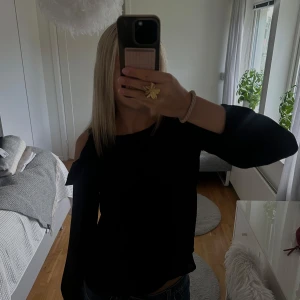 Svart blus med volang och öppna axlar - Säljer en svart blus från Cubus med snygga volangdetaljer på axlarna. Blusen har långa ärmar och är gjord i ett lätt, flowy material som känns skönt mot huden. Perfekt för dig som vill ha en stilren men ändå trendig look.