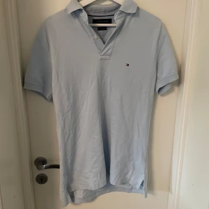 Ljusblå pikétröja Tommy Hilfiger  - Snygg ljusblå pikétröja från Tommy Hilfiger i bomull. Klassisk krage, korta ärmar och liten broderad logga på bröstet. Perfekt för en clean och avslappnad stil. Passar dig som gillar stilrena plagg. Storlek S bra skick