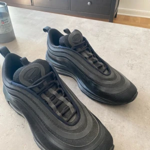 Nike Air Max 97  triple black -  Obs liten skråma påbild  3 på reflex linjen på sidan Nike Air Max 97 sneakers i svart med silvriga reflekterande detaljer och vågiga linjer längs ovansidan. Snygg design med rund tå, snörning och synlig Air-sula för extra komfort.  perfekt för dig som gillar streetwear och sportig stil. Nästan aldrig använda mvh