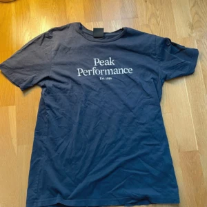 Blå Peak Performance t-shirt - Snygg mörkblå t-shirt från Peak Performance med vit logotyp och text 'Est. 1986' på bröstet. Klassisk rund hals och korta ärmar. Skön bomullskvalitet som passar perfekt till jeans eller shorts. Enkel och stilren design som alltid funkar.
