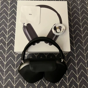 AirPod Max Svart - Bilderna visar ett par vita over-ear hörlurar med modern design och mjuka öronkuddar. Produkten levereras med ett skyddsfodral och originalförpackning. Perfekt för dig som älskar musik och vill ha stilrena hörlurar med hög komfort.
