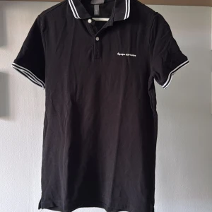 Svart pikétröja h&m - Svart pikétröja från h&m i storlek S. Klassisk krage med vita ränder och knappar framtill. Kortärmad modell med matchande vita ränder på ärmsluten. Broderad logga på bröstet. Perfekt för en clean och sportig look.