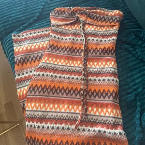 Färgglad långklänning med snörning - Säljer en långklänning i stickad stil med färgstarkt mönster i orange, brunt, vitt och lila. Klänningen har snygg snörning framtill och är axelbandslös. Perfekt för dig som vill sticka ut med coola mönster och boho-vibes.