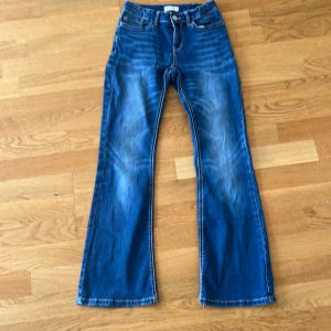 Blå bootcut jeans med hjärtdetalj - Snygga blå bootcut jeans med coola kontrastsömmar på bakfickorna och en söt hjärtpatch baktill. Jeansen har klassisk femficksdesign och är tillverkade i mjukt denimtyg. Perfekta för dig som gillar en retro vibe och vill sticka ut lite extra.