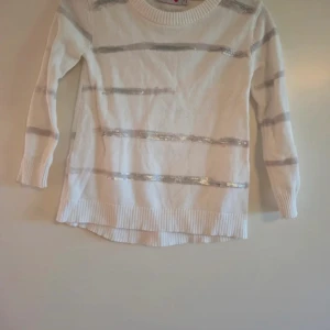 Vit randig tröja med silverdetaljer Boboli - Vit långärmad tröja från Boboli med silvriga paljettränder. Tröjan har rund hals, ribbade muddar och nederkant. Perfekt för dig som gillar lite extra bling i vardagen.