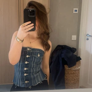 Jeanskorsett från Zara XS - Supersnygg jeanskorsett från Zara i  blå denim med silverfärgade knappar framtill och råa kanter nertill. Toppen är axelbandslös och har dekorativa fickor framtill samt smockad baksida för extra passform. Säljer då den inte kommer till anvädning längre