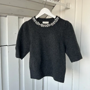 Mörkgrå stickad blus med pärlor Neo Noir - Supersnygg mörkgrå stickad blus från Neo Noir med korta puffärmar och glittrande pärldetaljer runt halsen. Materialmix av ull, polyester, akryl och elastan ger en mjuk och skön känsla. Perfekt för dig som vill ha något extra till hösten eller vintern. Ny pris 800!