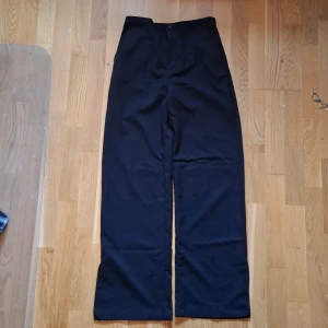 Svarta raka kostymbyxor från H&M, high waist - Svarta kostymbyxor från H&M med rak passform och hög midja. Byxorna har justerbar midja och är tillverkade i en mjuk blandning av polyester, viskos och elastan. Perfekta för en clean och stilren look.