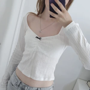 Vit långärmad topp från Gina Tricot - Supersöt vit långärmad topp från Gina Tricot med smala ribbade ränder och små hålmönster. Toppen har en croppad passform, v-ringning och en liten svart rosett framtill som detalj. Den är bara använd ca 2 gånger och är i väldigt bra skick! Jag säljer den eftersom att jag inte använder den. Jag köpte den för 260 kr.