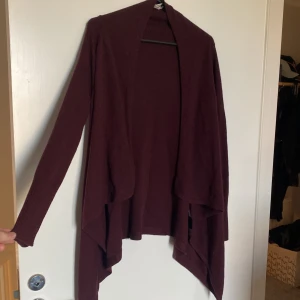 Vinröd omlottkofta från H&M XS - Säljer en vinröd kofta från H&M i storlek XS. Koftan har en snygg omlott-look med långa ärmar och fallande framstycken. Materialet är mjukt och stickat, perfekt för lager-på-lager under höst och vinter. Enkel att matcha med både jeans och leggings.