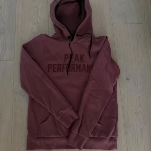 Vinröd hoodie Peak Performance - Säljer en vinröd hoodie från Peak Performance med tryckt logga på bröstet. Tröjan har huva med snörning, känguruficka och långa ärmar. Perfekt för dig som gillar en avslappnad och sportig stil. Använd 1 gång. Storlek S men passar S/XS. Kan mötas på Ekerö annars står köparen för frakten.