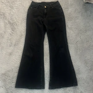 Svarta bootcut jeans med utsvängda ben - Säljer ett par svarta jeans med bootcut och riktigt utsvängda ben. Klassisk femficksmodell med hällor för bälte och knappstängning. Jeansen har en snygg mörk tvätt och raka sömmar, perfekta för dig som gillar retrovibbar.
