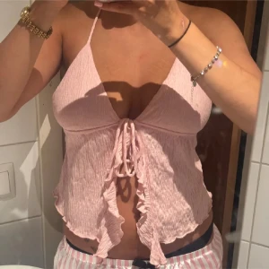 Ljusrosa volangig halterneck topp - Supersöt ljusrosa linnetopp med volangkant och knyt framtill. Tunt tyg och halterneck med smala band som knyts i nacken. 