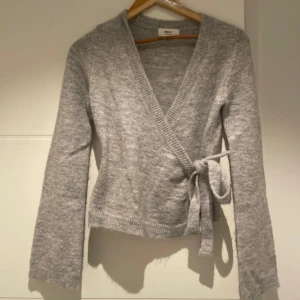 Grå omlottkofta med knyt - Supermjuk grå omlottkofta från Gina tricot med knyt i sidan och v-ringad hals. Långärmad och ribbade muddar vid ärmslut och nederkant. Perfekt att slänga på sig när det är lite kyligt ute. Man kan även ha ett linne under . 