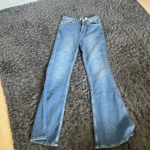 Blå flare jeans med hjärtformade bakfickor - Säljer ett par blåa flare jeans från H&M med hög midja och justerbar midja. Jeansen har unika hjärtformade bakfickor som ger en söt och trendig vibe. Tillverkade i klassiskt denimtyg och perfekta för dig som vill sticka ut lite extra.