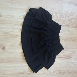 Svart volangkjol från h&m  - Supersöt svart kortkjol med bred smock i midjan och volangdetaljer. Kjolen har en luftig och flowy känsla, perfekt för att skapa en cool och avslappnad look. Passar dig som gillar att sticka ut med volanger och enkel stil. Storlek xs! Säljs då den ej används 