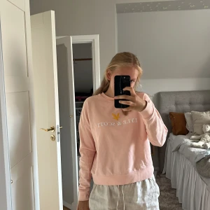Ljusrosa sweatshirt från Lyle & Scott - Säljer en ljusrosa sweatshirt från Lyle & Scott med vit logga och gul fågel framtill. Tröjan har rund hals, långa ärmar och en relaxed passform. Perfekt för dig som gillar en enkel men snygg stil.