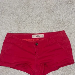 Lågmidjade röda shorts från Hollister - Snygga lågmidjade röda shorts från Hollister med klassisk femficksdesign och knappstängning framtill. De har bälteshällor, två bakfickor och en liten Hollister-logga broderad på baksidan. Perfekta för varma dagar och snygg modell dessutom! Storlek 27! Varan säljs på andra plattformar💕