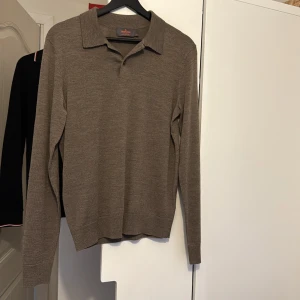 Brun pikétröja i merinoull från Morris - Snygg brun pikétröja från Morris i 100% merinoull. Tröjan har klassisk krage och lång ärm, perfekt för dig som gillar stilrena och bekväma plagg. Passar dig som vill ha en enkel men sofistikerad look. Färgen är neutral och lätt att matcha med andra kläder.