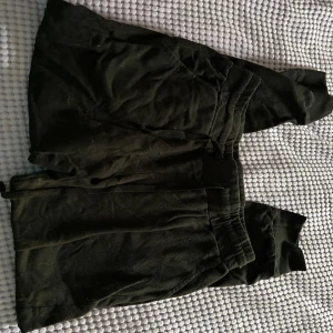 Svarta mjukisbyxor med GAME OVER-tryck - Svarta mjukisbyxor med snörning. På ena benet finns ett vitt GAME OVER-tryck i retro gaming-stil. Byxorna har muddar vid bensluten och är gjorda i mjukt material, perfekta för chill eller gaming.