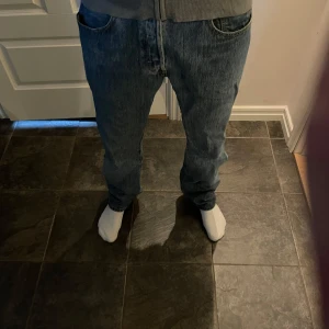 Levi's 501 blå jeans straight fit - Klassiska Levi's 501 jeans i blå denim med rak passform och knappgylf. Snygg vintagekänsla och tidlös look, perfekta till sneakers eller boots. Hög midja och femficksmodell, tillverkade i bomull för en autentisk jeanskänsla.