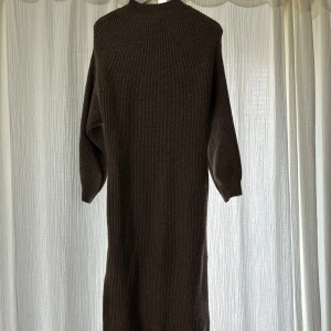 Brun stickad långklänning H&M - Mysig brun ribbstickad långklänning från H&M L.O.G.G. med hög hals och långa ärmar. Klänningen har en rak passform och en slits på sidan för extra rörelsefrihet. 