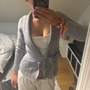 Grå stickad kofta med knytband - Vintage från veromoda. Mysig grå stickad kofta med bred ribbad krage och knytband i midjan. Perfekt att slänga på sig över ett linne nu när det blir kallare.