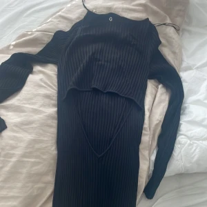 Svart ribbad långklänning från Guess - Svart långklänning från Guess med ribbad struktur och snygga sömdetaljer som skapar ett V-mönster framtill. Klänningen har lång ärm och en tight passform som framhäver figuren. Perfekt för dig som gillar stilrena och moderna plagg med en edge. Köpt för 1350 men säljer för 550 prislapp står kvar