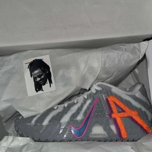 Nike sneakers med zebra-mönster - Unika Nike sneakers med grått och vitt zebramönster, färgglada detaljer som en rosa och blå swoosh samt en stor orange bokstav A på sidan. Skorna har platt sula och snörning, tillverkade i mesh och syntetmaterial. Perfekta för dig som vill sticka ut.