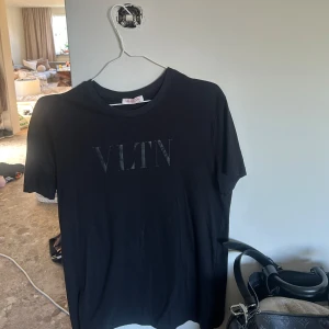  VLTN T-shirt - Svart t-shirt från Valentino med VLTN-tryck på bröstet. Klassisk rund hals och korta ärmar, perfekt för en clean och stilren look. Mjuk bomull som känns skön mot huden. Passar dig som gillar designer och enkel stil.