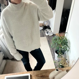 Beige stickad polotröja - Säljer en mysig beige stickad polotröja med hög krage och långa ärmar. Tröjan har en loose passform och är tillverkad i ett mjukt, strukturerat material som känns skönt mot huden. Perfekt för att hålla sig varm under kyliga dagar. Ens armen har slitits upp men går enkelt att sy ihop.