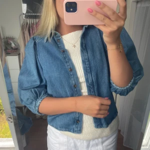 Blå jeansjacka med puffärm - Säljer en snygg blå jeansjacka med puffiga trekvartsärmar och knappar framtill. Jackan har en loose fit och är tillverkad i klassiskt denimtyg. Perfekt att slänga över en topp för en chill och trendig look. Helt oanvänd! Storlek M men skulle säga att den passar mer storlek S