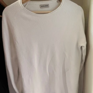 Vit långärmad tröja Jack & Jones - Snygg vit långärmad tröja från Jack & Jones i bomull. Tröjan har en rund halsringning och diskret struktur i tyget som ger en stilren look. Perfekt att matcha med jeans eller chinos för en clean outfit.