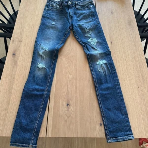 Blå slitna skinny jeans från Jack&Jones - Säljer ett par blå skinny jeans från Jack&Jones med slitningar och hål på benen. Klassisk femficksmodell med låg midja och smal passform. 