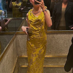 Guldfärgad långklänning med blommönster från Zara - Säljer en maxad guldig långklänning från Zara med blommigt mönster och snygg draperad halsringning. Klänningen har öppen rygg och är ärmlös, vilket ger en riktigt chic vibe. Materialet är glansigt och känns lyxigt, perfekt för att sticka ut. Passformen är normal.